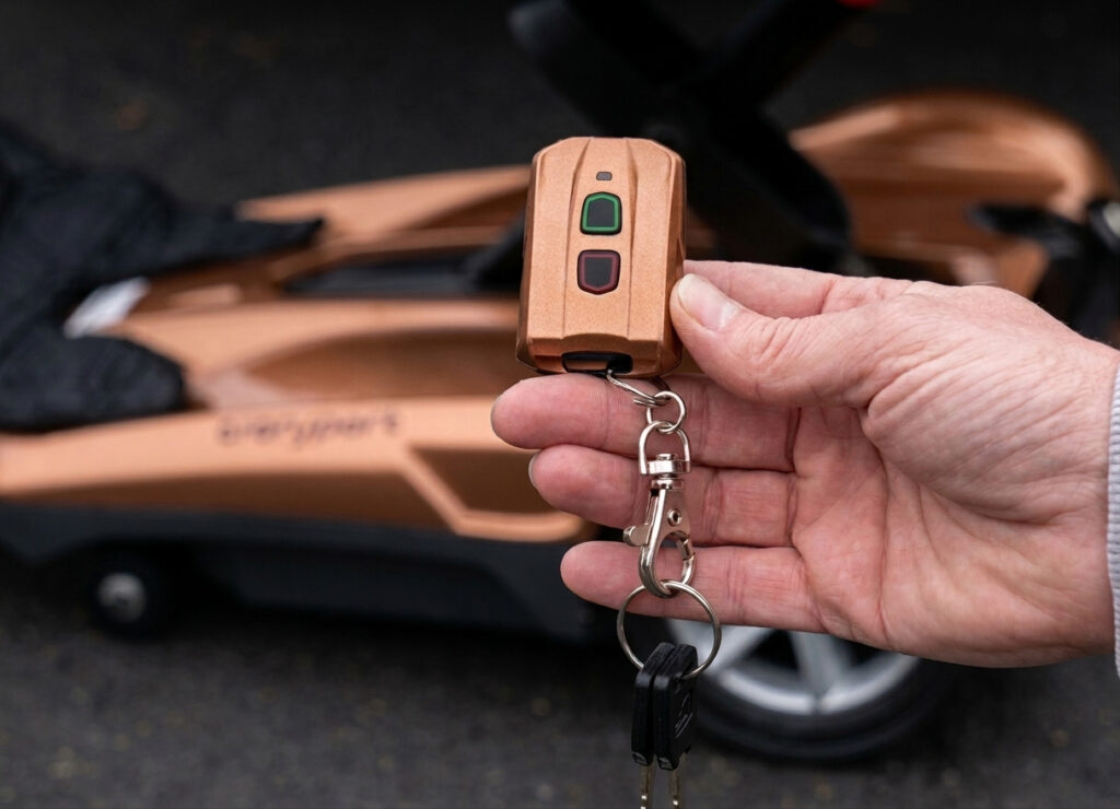 A hand demonstrates the compact remote key fob for the EV Rider Transport AF+ folding mobility scooter.
