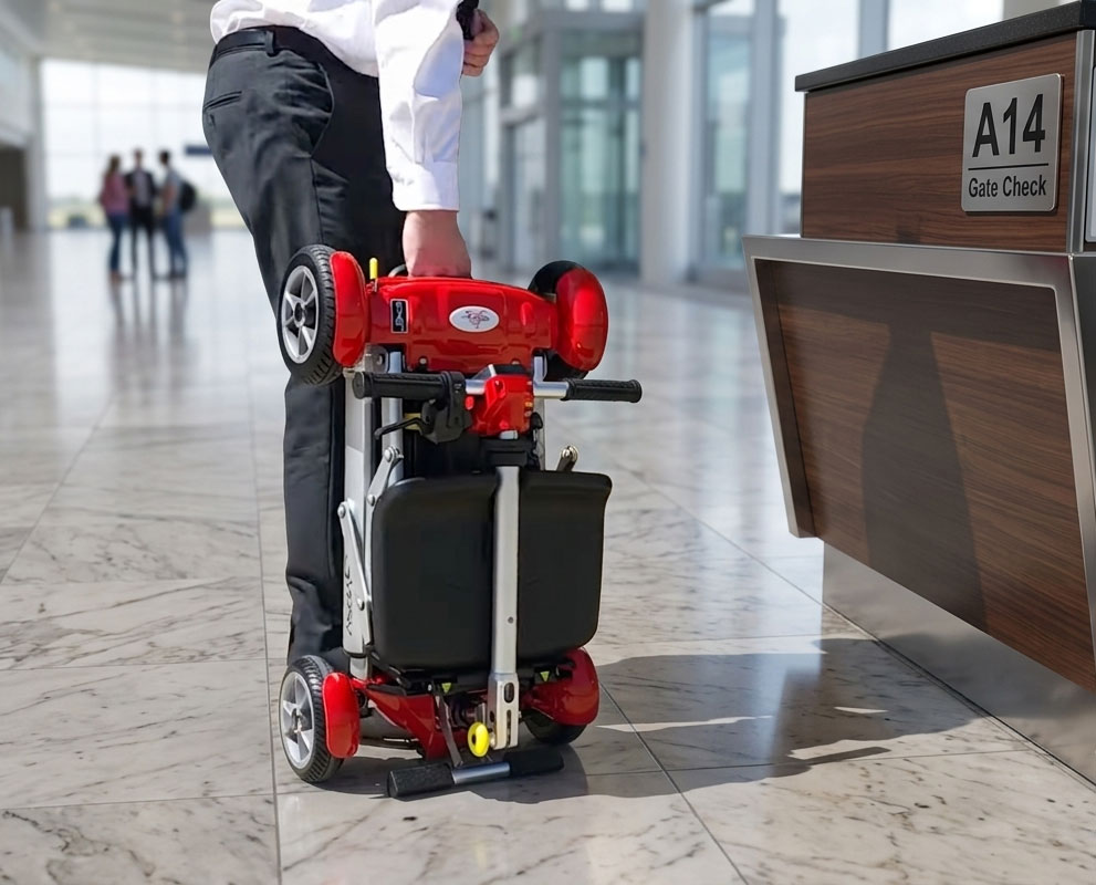 A person effortlessly lifting a compact, fully folded red EV Rider Gypsy Q2 mobility scooter by its frame in a modern terminal lobby.